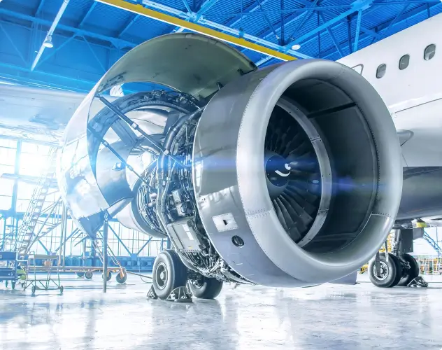 A close-up view of an aircraft jet engine undergoing maintenance in a brightly lit hangar.