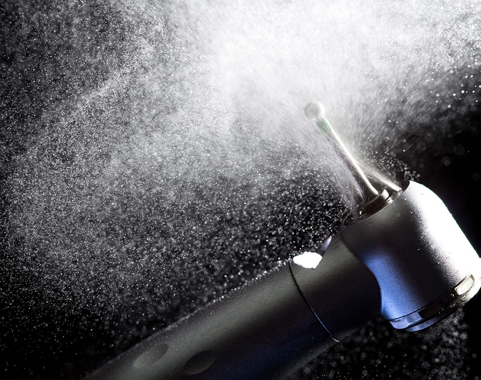 Dental handpiece drill spraying water mist during high-speed operation.